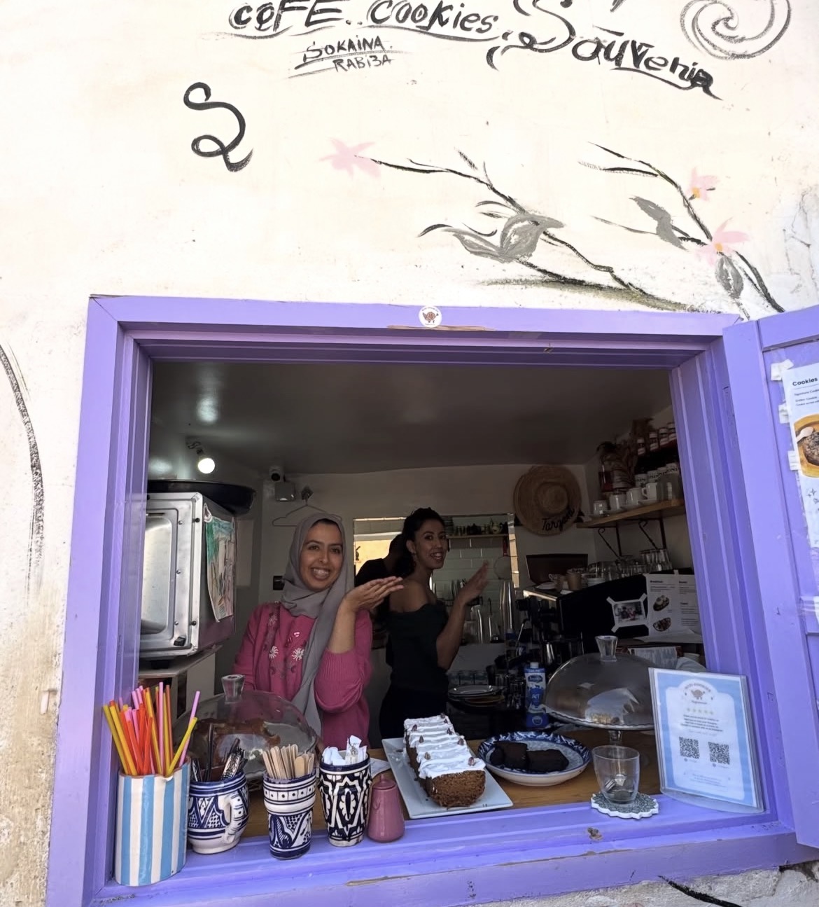 The sisters at their actual shop window with the review poster on the counter